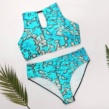 Load image into Gallery viewer, A two-piece bikini set with a turquoise, gray, and white abstract camouflage pattern, laid flat on a white surface with decorative green leaves 