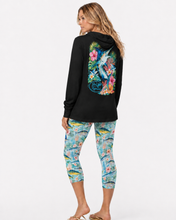 Load image into Gallery viewer, A woman shown from the back wearing a black long-sleeve reel mermaid tropical marlin hoodie and matching multicolor floral capri leggings, against a plain light gray studio background.